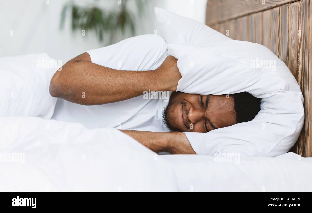 Uomo disturbato che copre le orecchie con cuscino sofferente da Insomnia Indoor Foto Stock