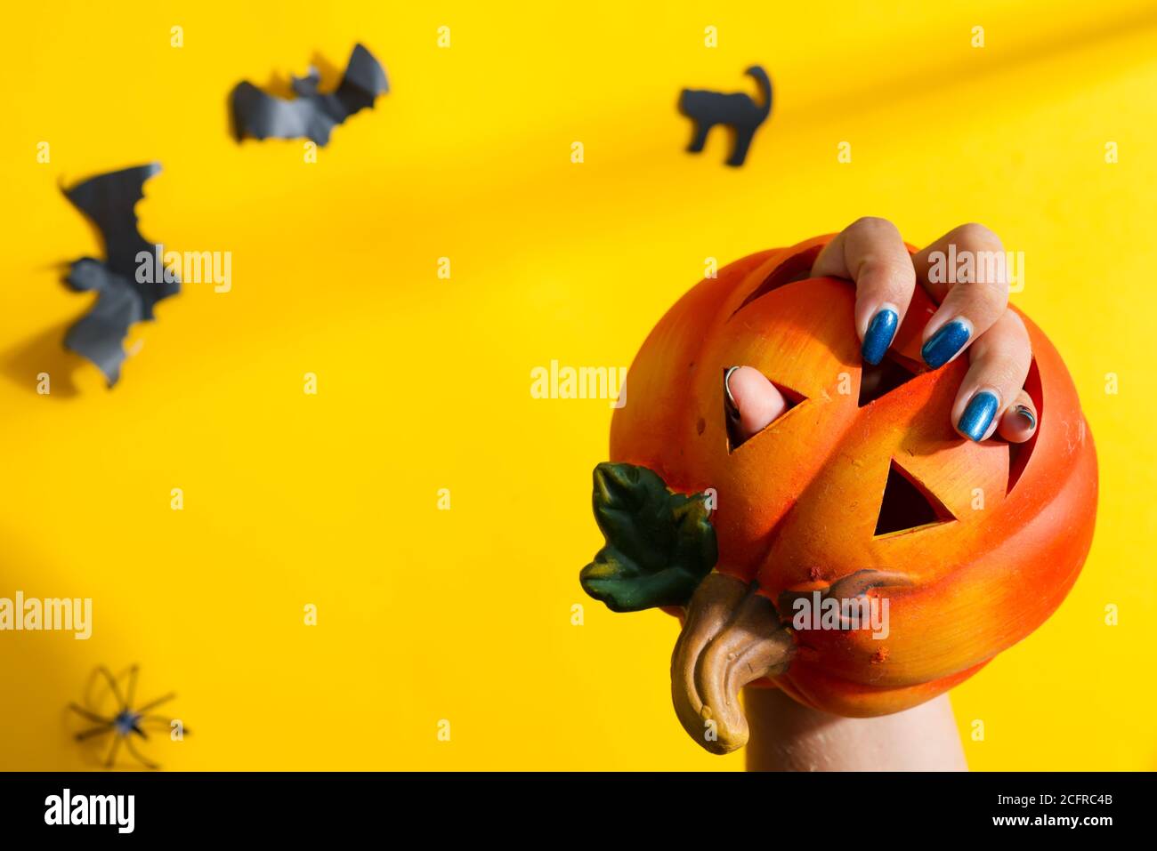 La mano della donna sta tenendo la zucca decorazione di Halloween sopra lo sfondo giallo con i pipistrelli neri tagliati a mano, spazio di copia. Foto Stock