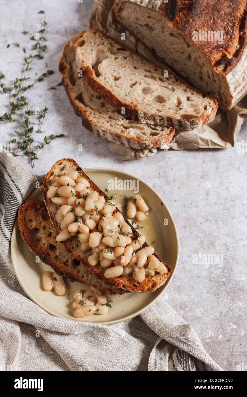 Fagioli cannellini cotti su pane tostato con timo fresco e pane affettato. Foto Stock