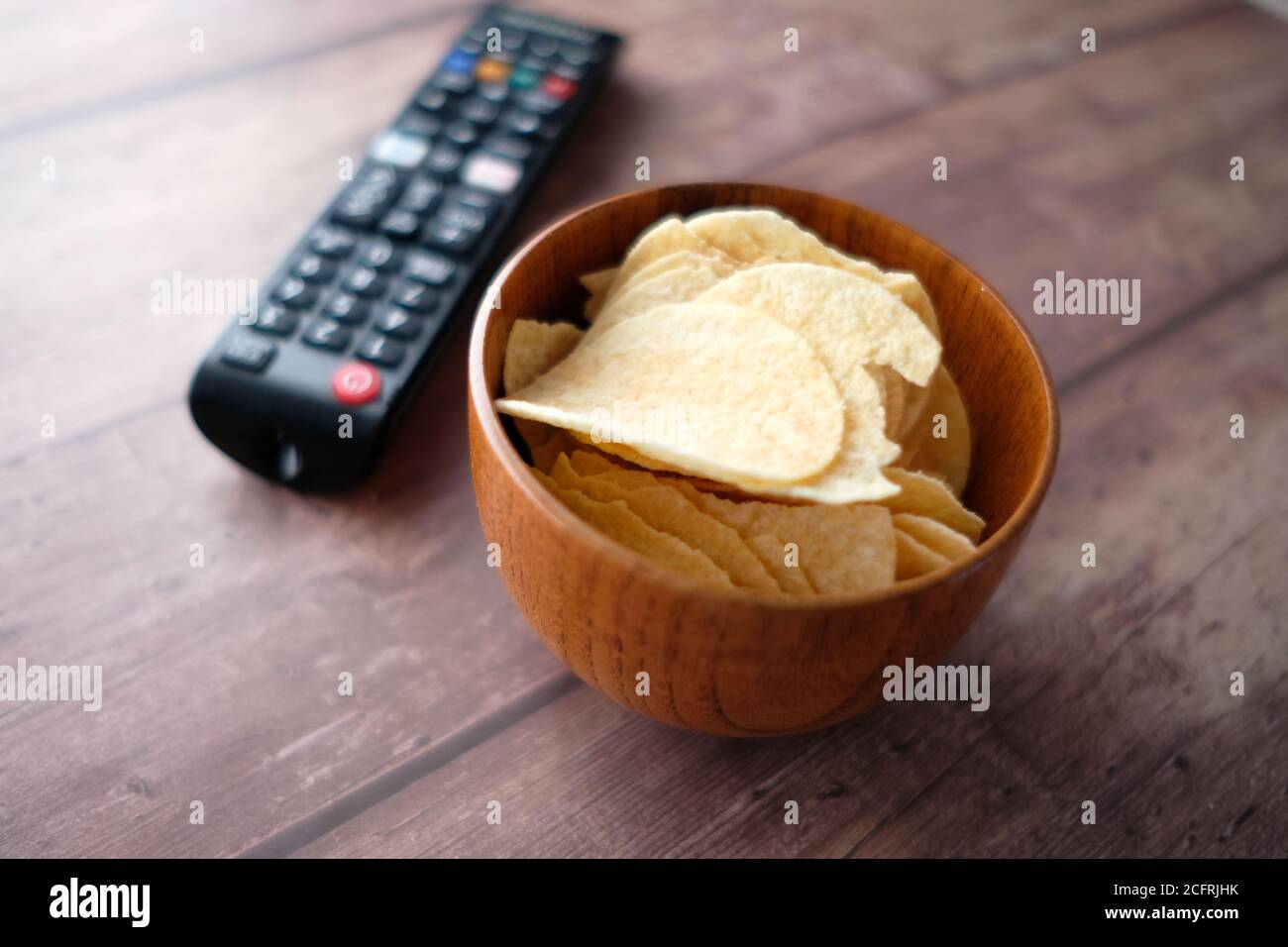 ciotola di patatine e telecomando tv su sfondo di legno. Foto Stock