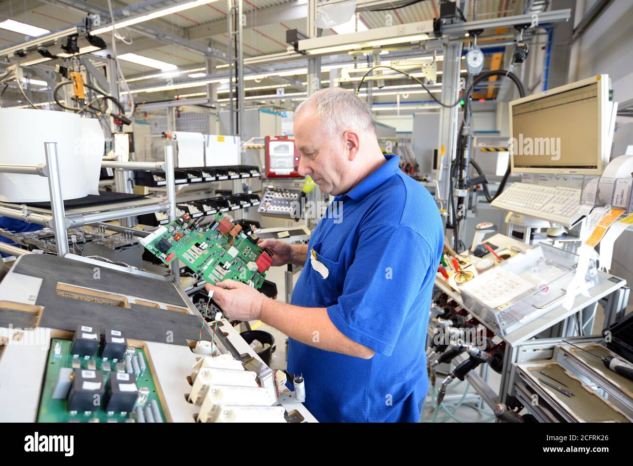 un lavoratore più anziano e amichevole di un'azienda industriale assembla componenti elettronici nell'ingegneria meccanica di una fabbrica moderna Foto Stock
