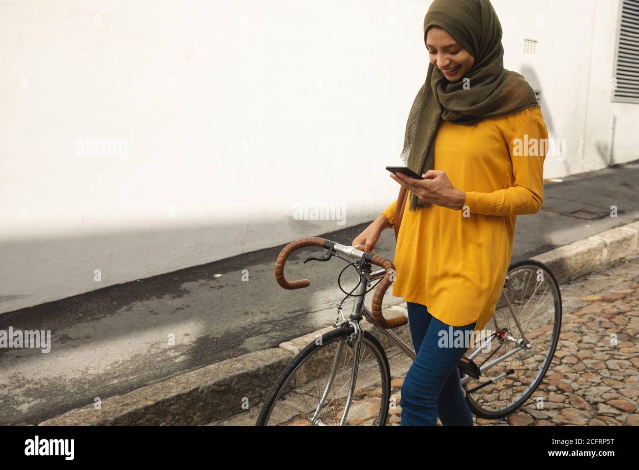 Donna in hijab con smartphone mentre si cammina in bicicletta Foto Stock