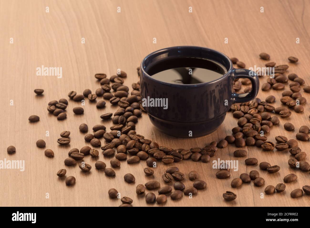 tazza blu con espresso e circa con i chicchi di caffè intorno, su un tavolo di legno, studio Foto Stock