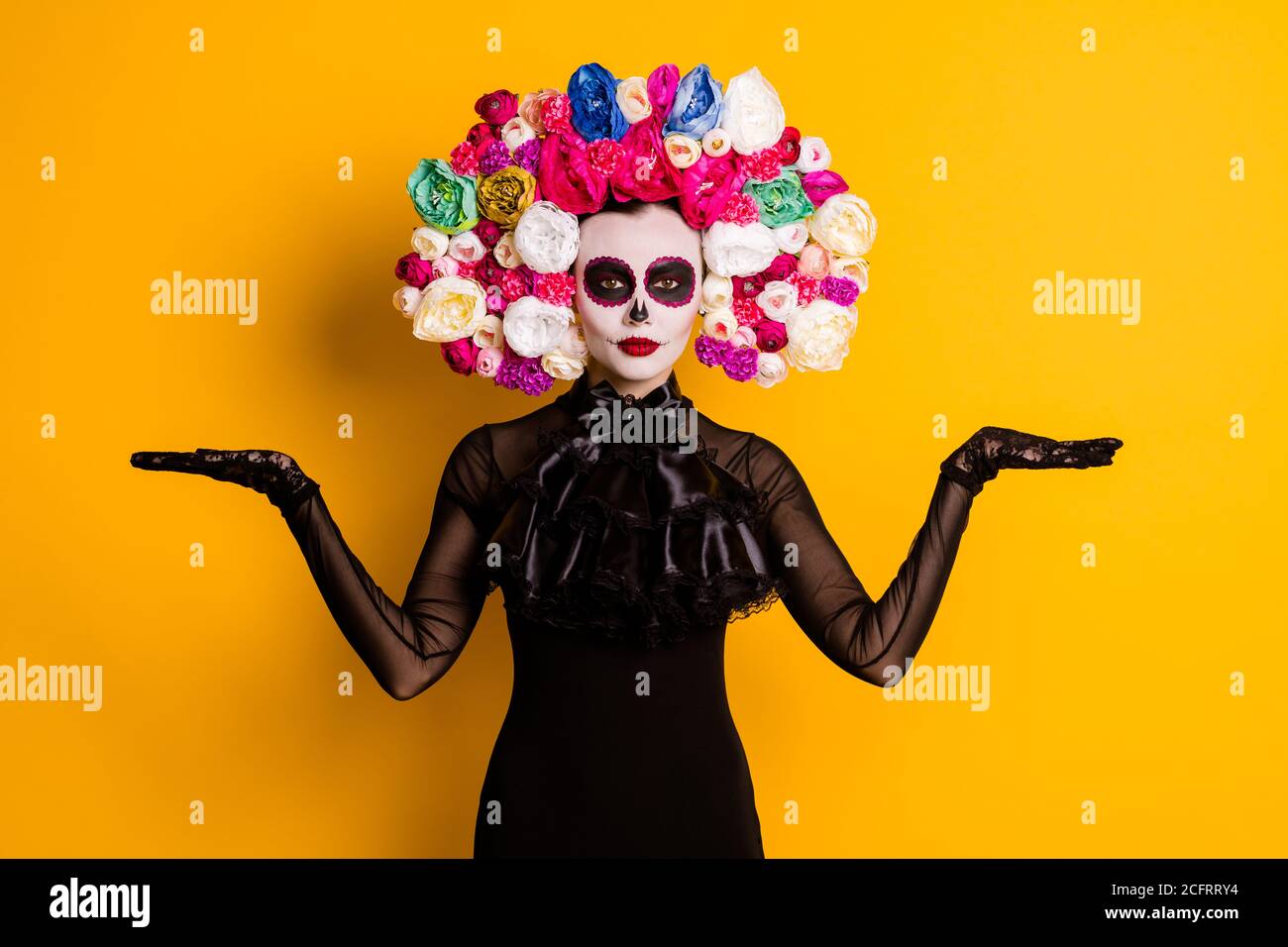 Foto di simpatica giovane signora paurosa guardare le mani tenere spazio vuoto proporre speciali oggetti tradizionali indossare abito nero morte rose in costume di carnevale Foto Stock