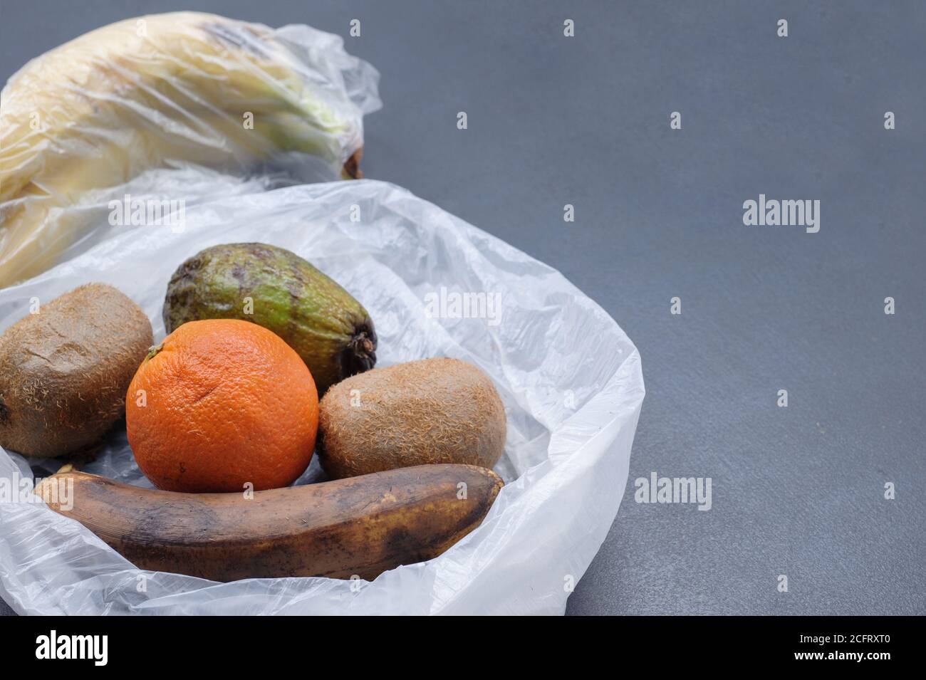 Frutta rovinata nel sacchetto di plastica su sfondo grigio. Spazzatura discarica cibo marcio. Concetto di zero sprechi. Immagine con spazio di copia, orizzontale. Foto Stock