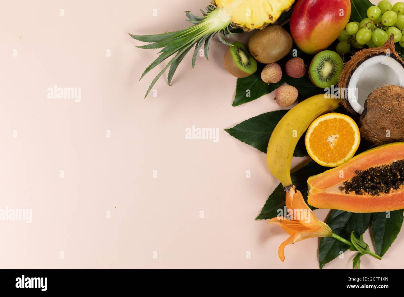Vista di una composizione con varietà di frutta tropicale fresca e foglie disposte su una superficie rosa Foto Stock