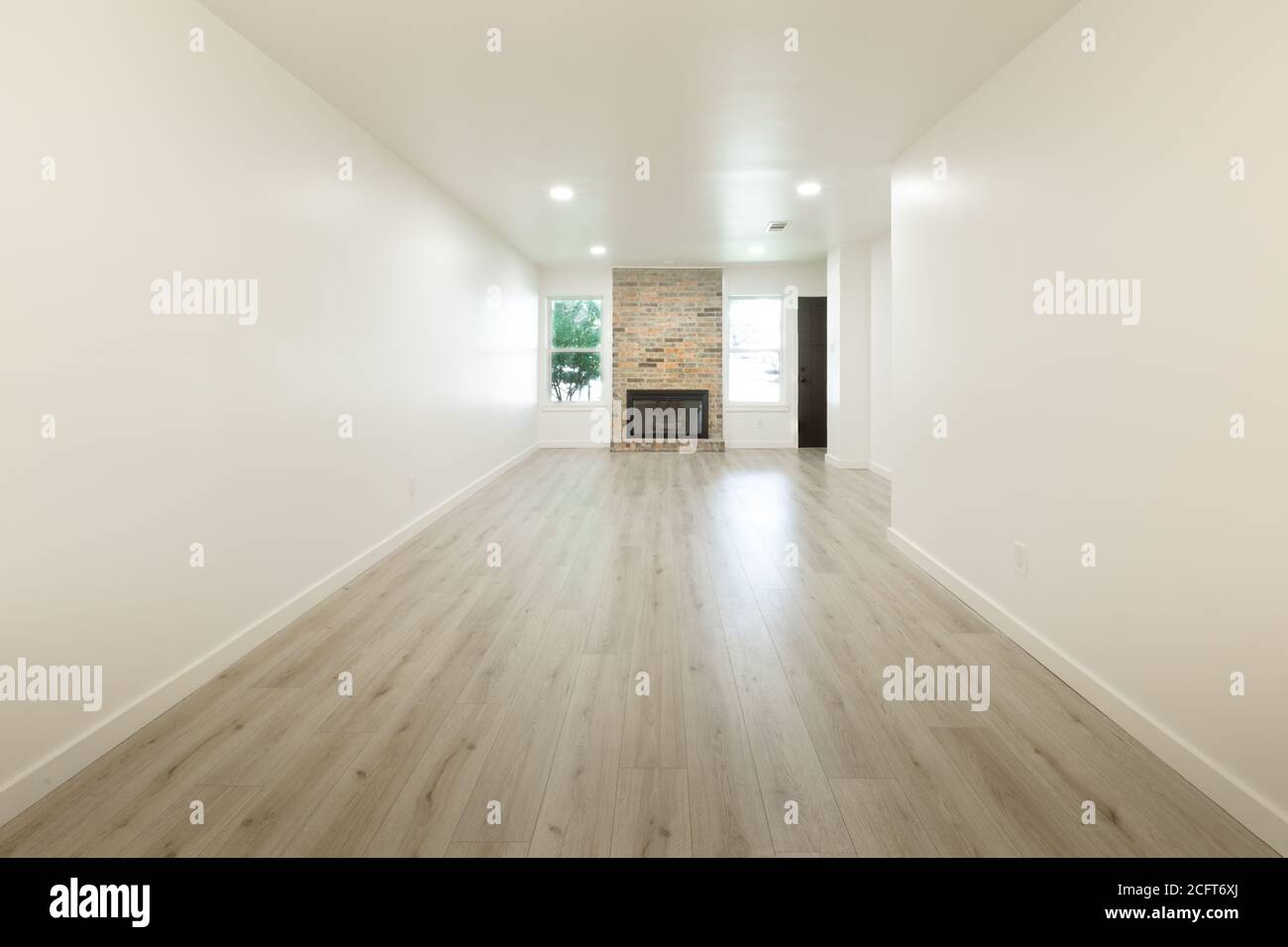 Soggiorno vuoto con camino, pareti bianche e pavimento in legno Foto Stock