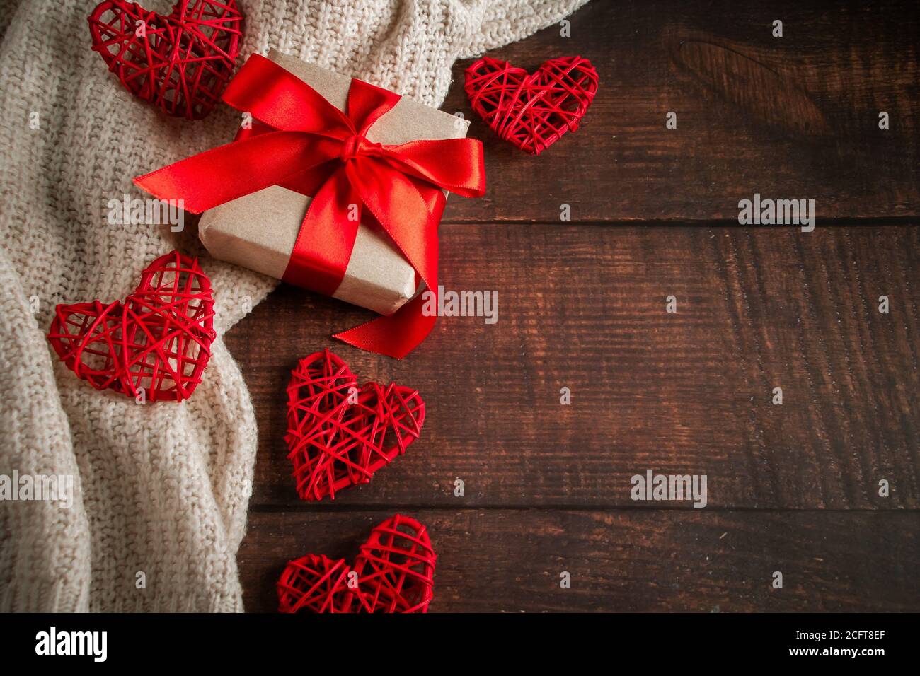 Regalo di San Valentino in una scatola con un nastro rosso su sfondo marrone. Confezione regalo in carta artigianale con nastro rosso per San Valentino. Cuori fatti a mano Foto Stock