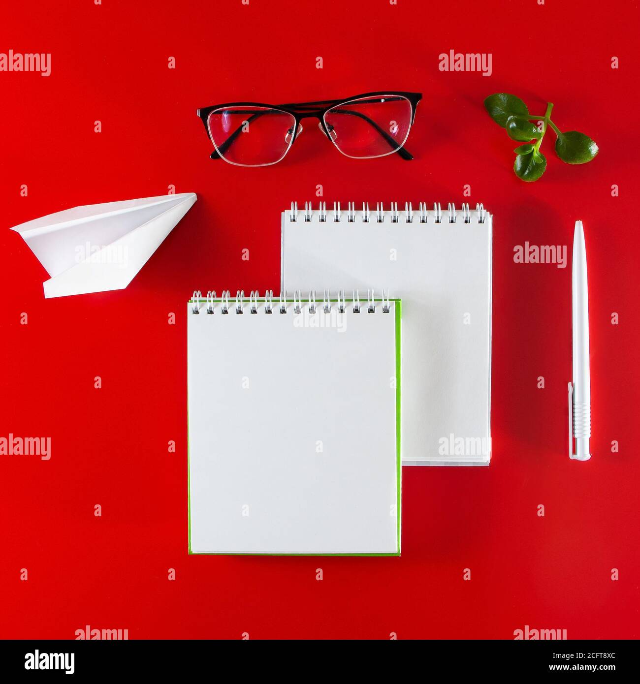 Materiali di consumo per ufficio su sfondo rosso. Notebook, penna e occhiali vuoti. Layout per il design nello stile del minimalismo. Foto Stock