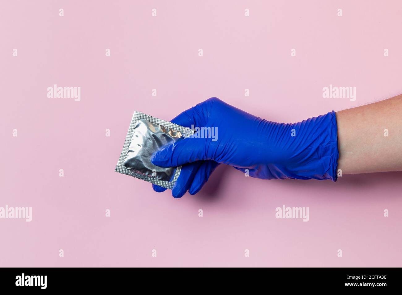 Una mano in un guanto di lattice blu tiene un preservativo. Il concetto di protezione preventiva contro il coronavirus. Assistenza sanitaria durante una pandemia. Foto Stock