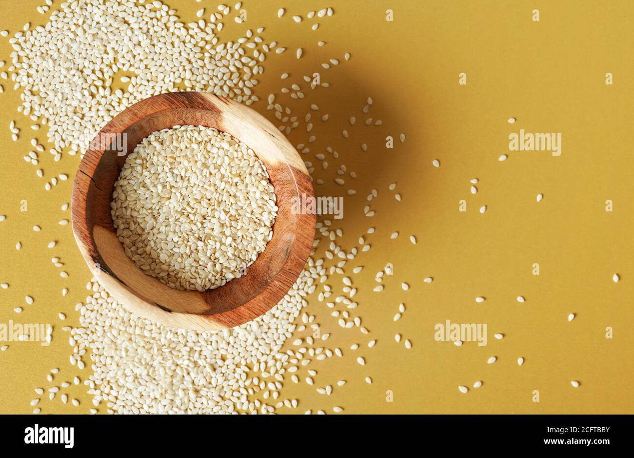 Minuscoli semi di sesamo bianchi in una piccola ciotola di legno, sulla scrivania gialla, vista dall'alto Foto Stock