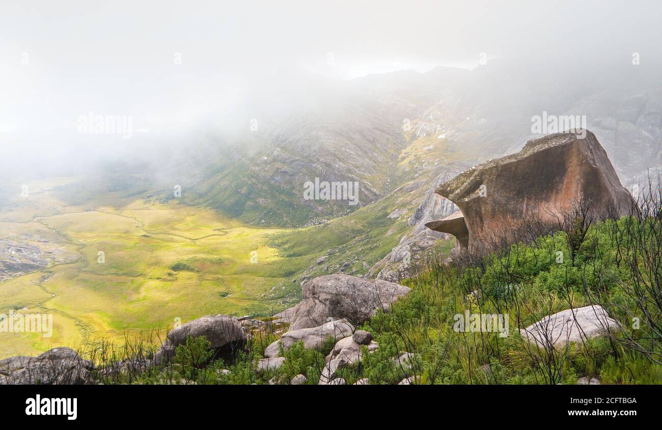 Paesaggio tipico visto durante il trekking al Bosy pic nel massiccio di Andringitra, Madagascar, la valle illuminata dal sole giù, un po 'di erba, cespugli e grande masso in Foto Stock