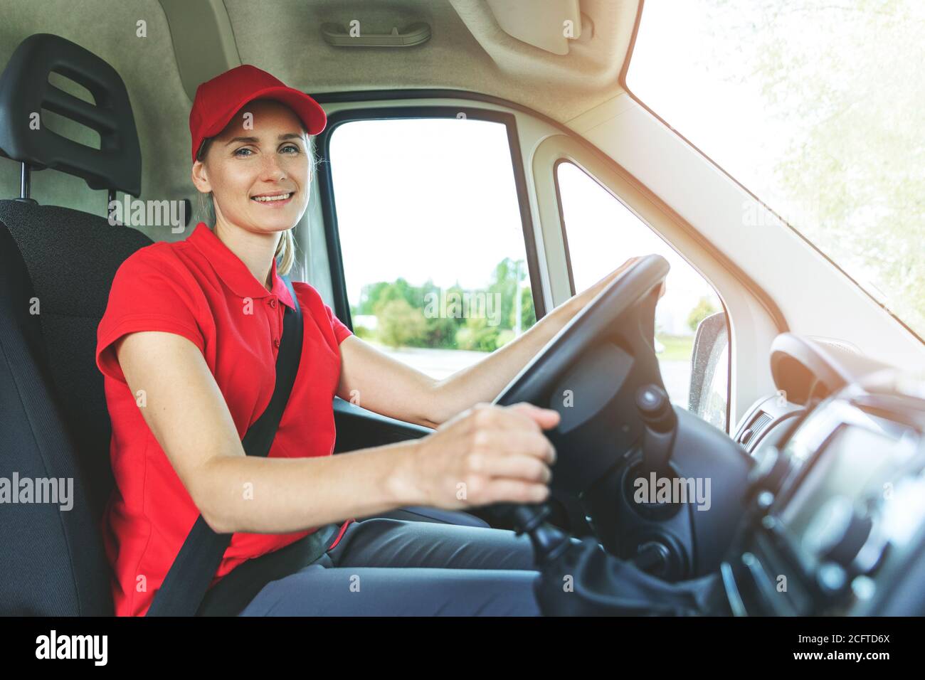 servizi di trasporto - giovane autista donna in uniforme rossa che guida un furgone. sorridendo alla macchina fotografica Foto Stock