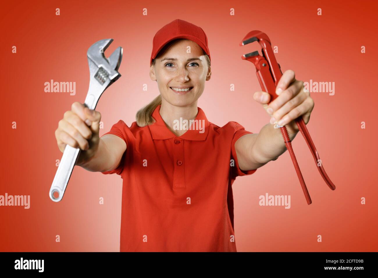 handyman services - donna maneggevole in uniforme rossa con riparazione strumenti in mani su sfondo rosso Foto Stock