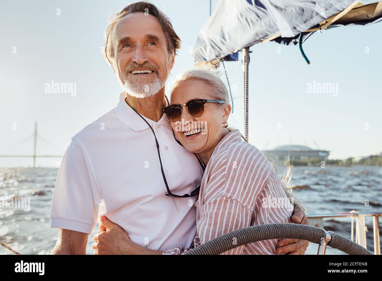 Coppia anziana allegra in piedi al volante su uno yacht e abbracciarsi l'un l'altro. Gente felice che gode di una giornata di sole su una barca. Foto Stock