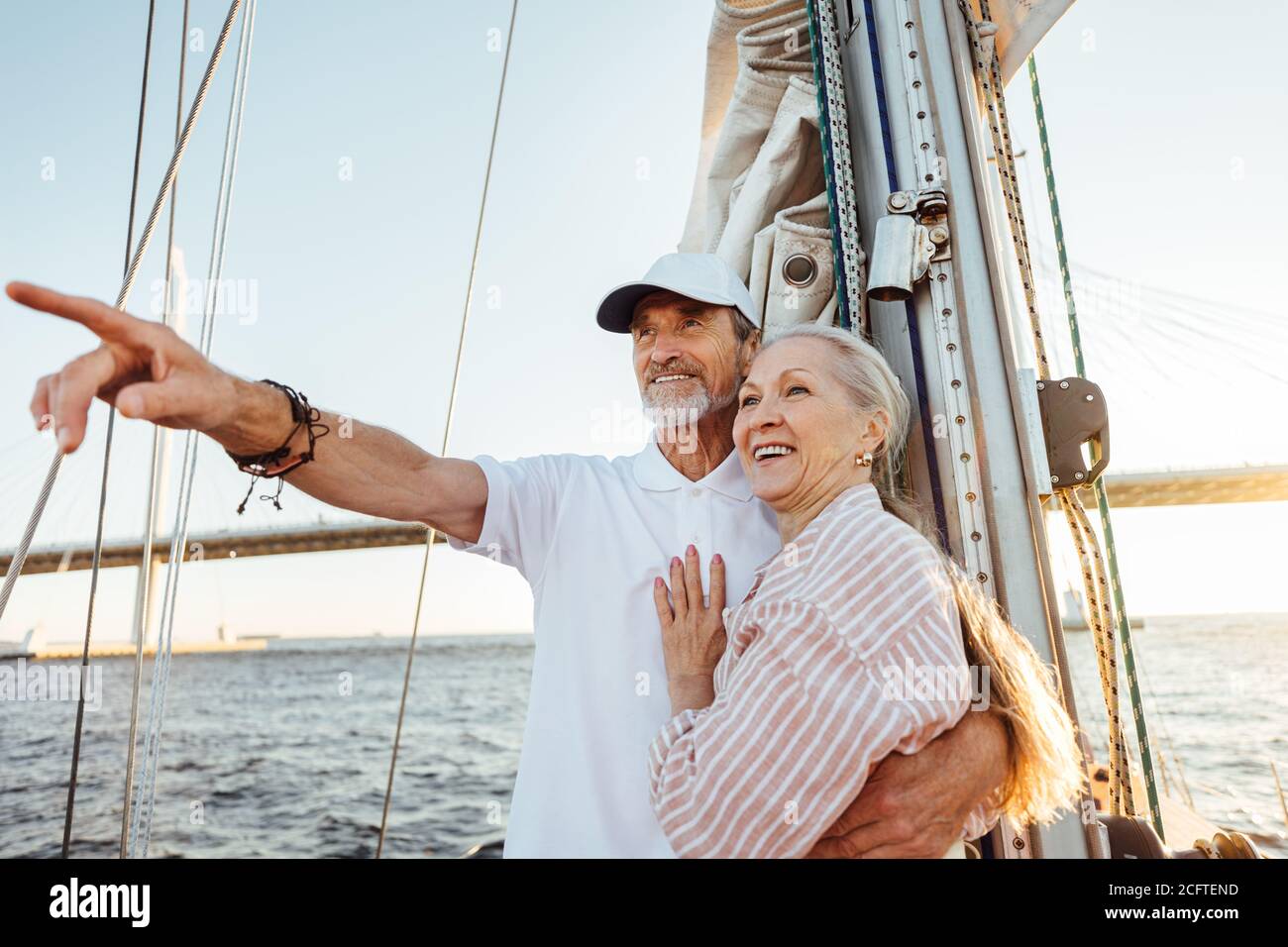Uomo maturo che indica la distanza e abbracciando sua moglie. Due persone sorridenti che si godono una gita in barca al tramonto. Foto Stock