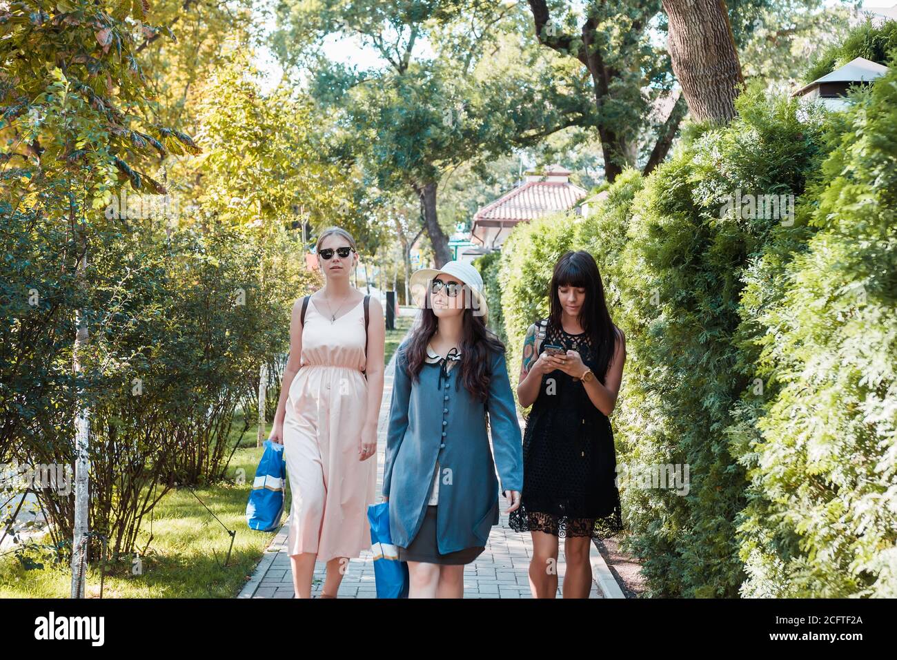 Tre belle giovani donne che camminano nel parco estivo dopo lo shopping. Gruppo di persone internazionali. Foto Stock