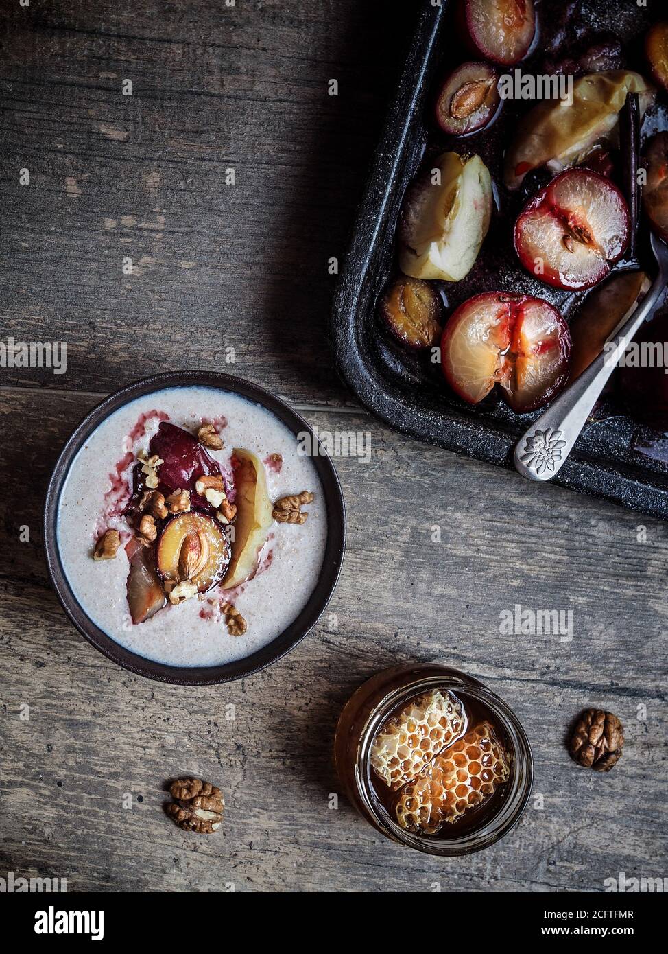 Prugne arrostite, gregoli rossi e mele su teglia da forno. Porridge di grano saraceno con frutta e noce in ciotola. Miele su tavola di legno. Vista dall'alto. Foto Stock