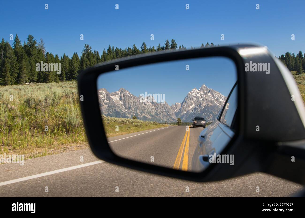 Una vista del Parco Nazionale del Grand Teton nella Specchietto retrovisore di un'auto che guida in Wyoming Foto Stock