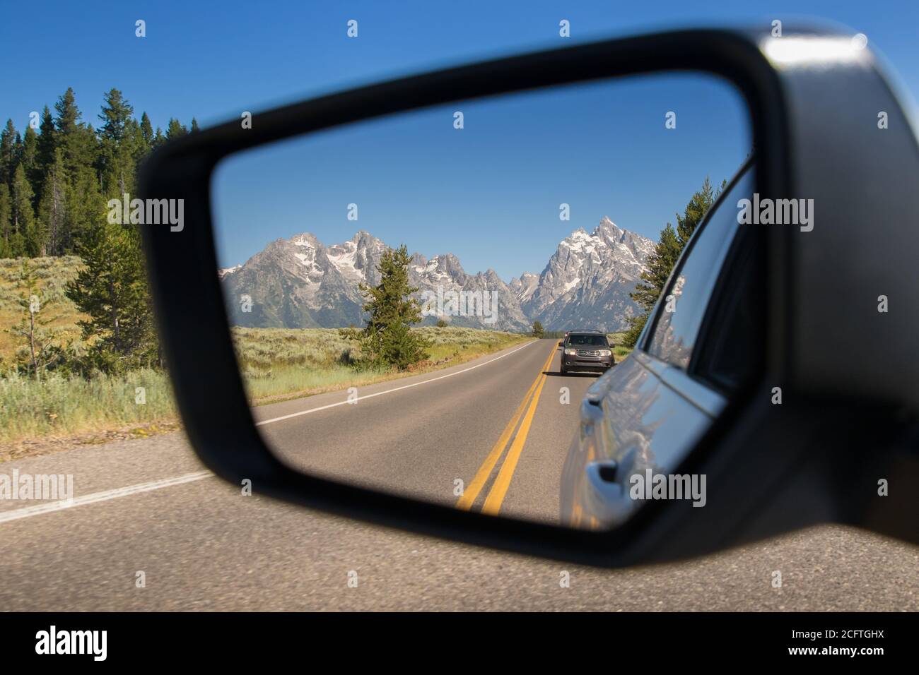 Una vista del Parco Nazionale del Grand Teton nella Specchietto retrovisore di un'auto che guida in Wyoming Foto Stock