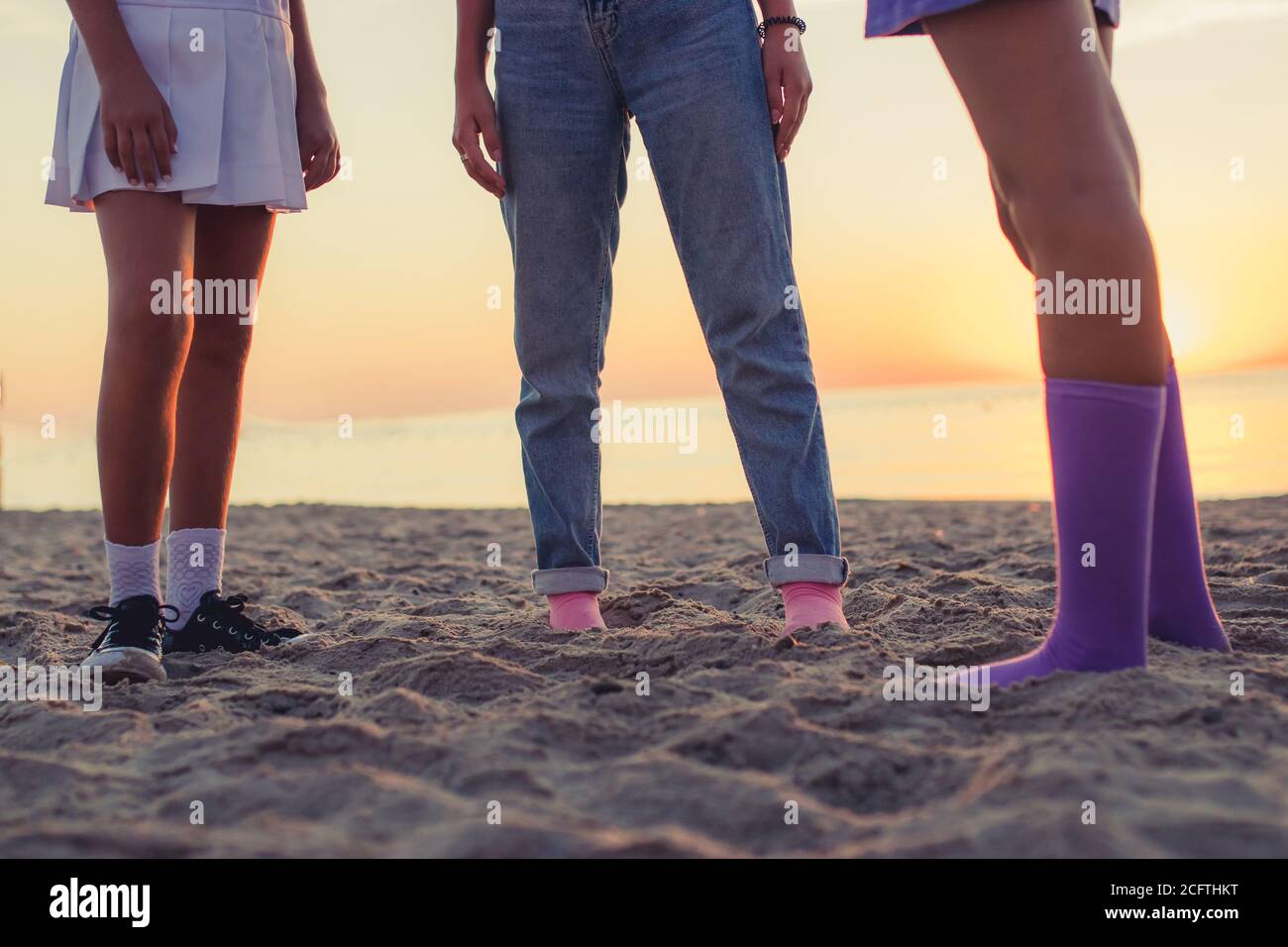 tre giovani amiche in piedi sulla spiaggia e guardando il mare all'alba. primi piani gambe Foto Stock