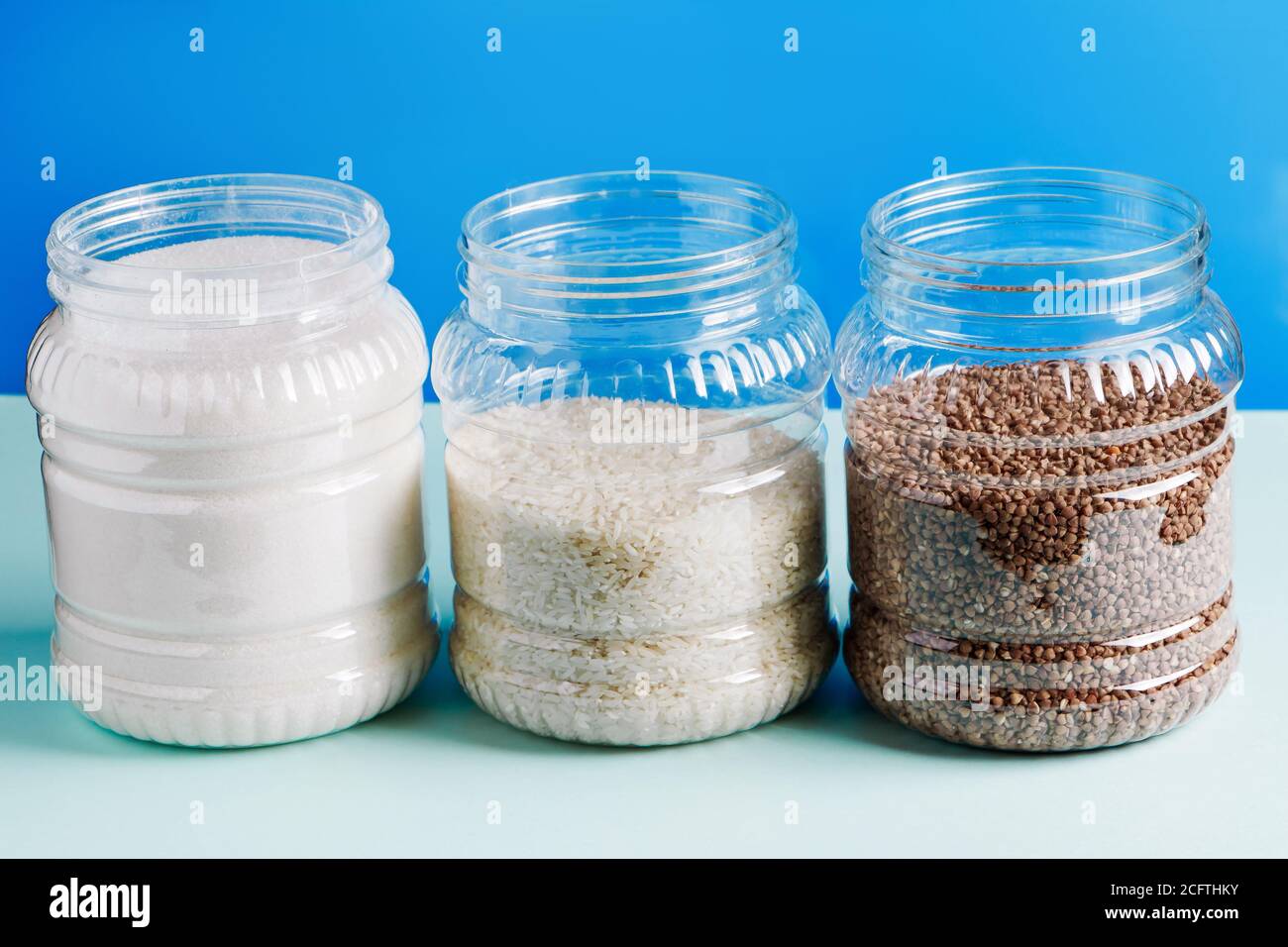 Vasi con cereali e zucchero su sfondo blu. Articoli essenziali per lo shopping in quarantena. Foto Stock
