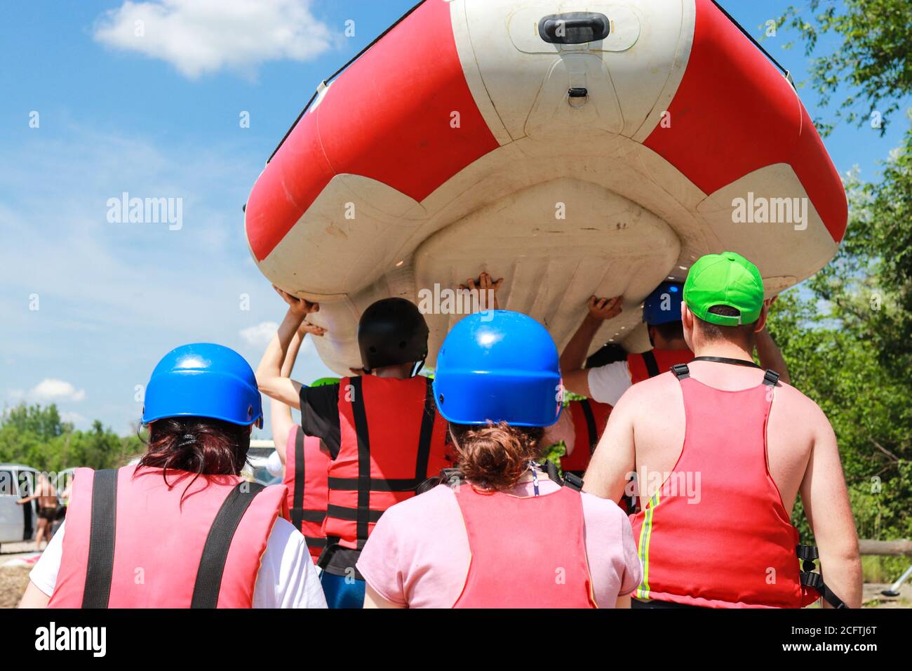 Squadra di rafting in attrezzature sportive dopo un rafting riuscito lungo il fiume trasporta una barca gonfiabile di gomma sopra al posizionare il punto in cui inizia la lega Foto Stock