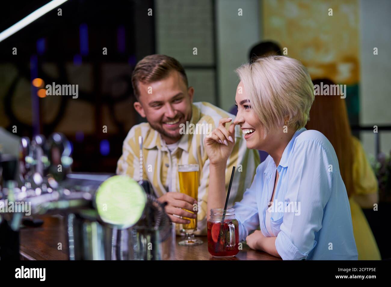 la ragazza ama le barzellette di uno straniero, ragazzo caucasico flirt con la ragazza bionda in un pub o bar Foto Stock