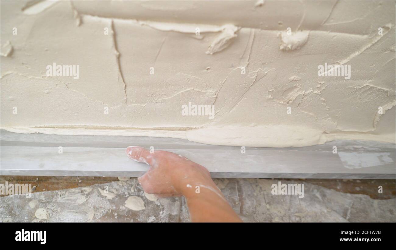 Lo strumento Provila viene applicato alla parete. La soluzione viene applicata alla parete con un attrezzo speciale. Lavoratore applicato con una spatola a una soluzione di Foto Stock