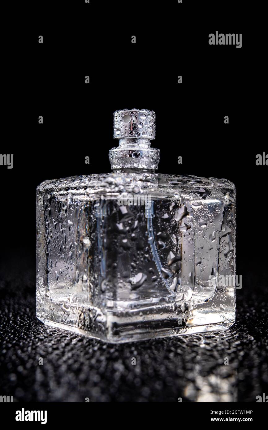 Contenitore in vetro con profumo coperto da gocce d'acqua. Una bottiglia bagnata con un atomizzatore. Sfondo scuro. Foto Stock