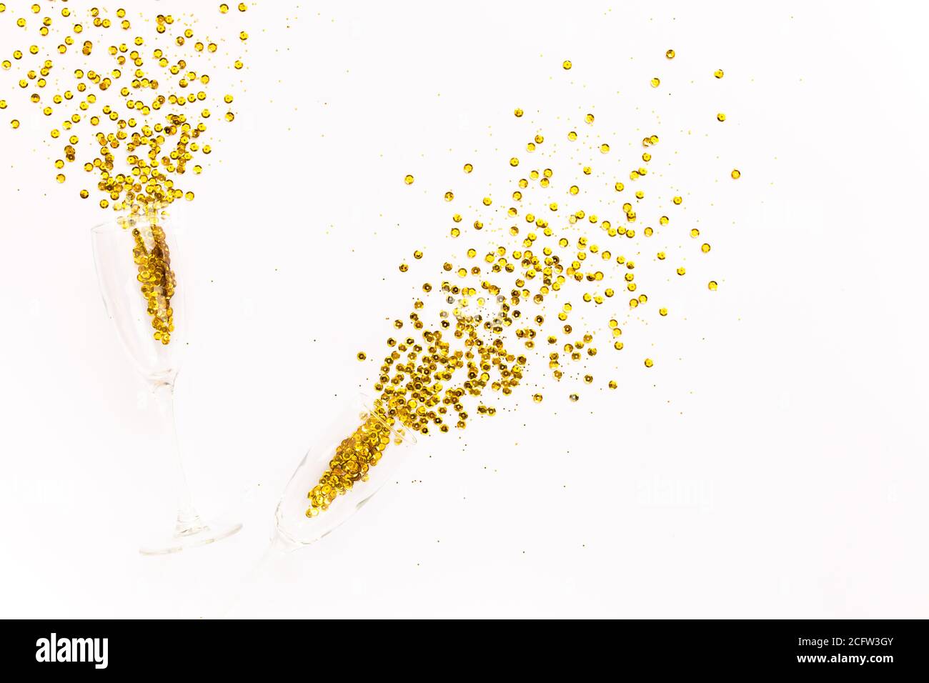Bicchieri di champagne con una spilla di confetti dorati su sfondo bianco. Piatto, vista dall'alto, festeggia il concetto di festa. Foto Stock
