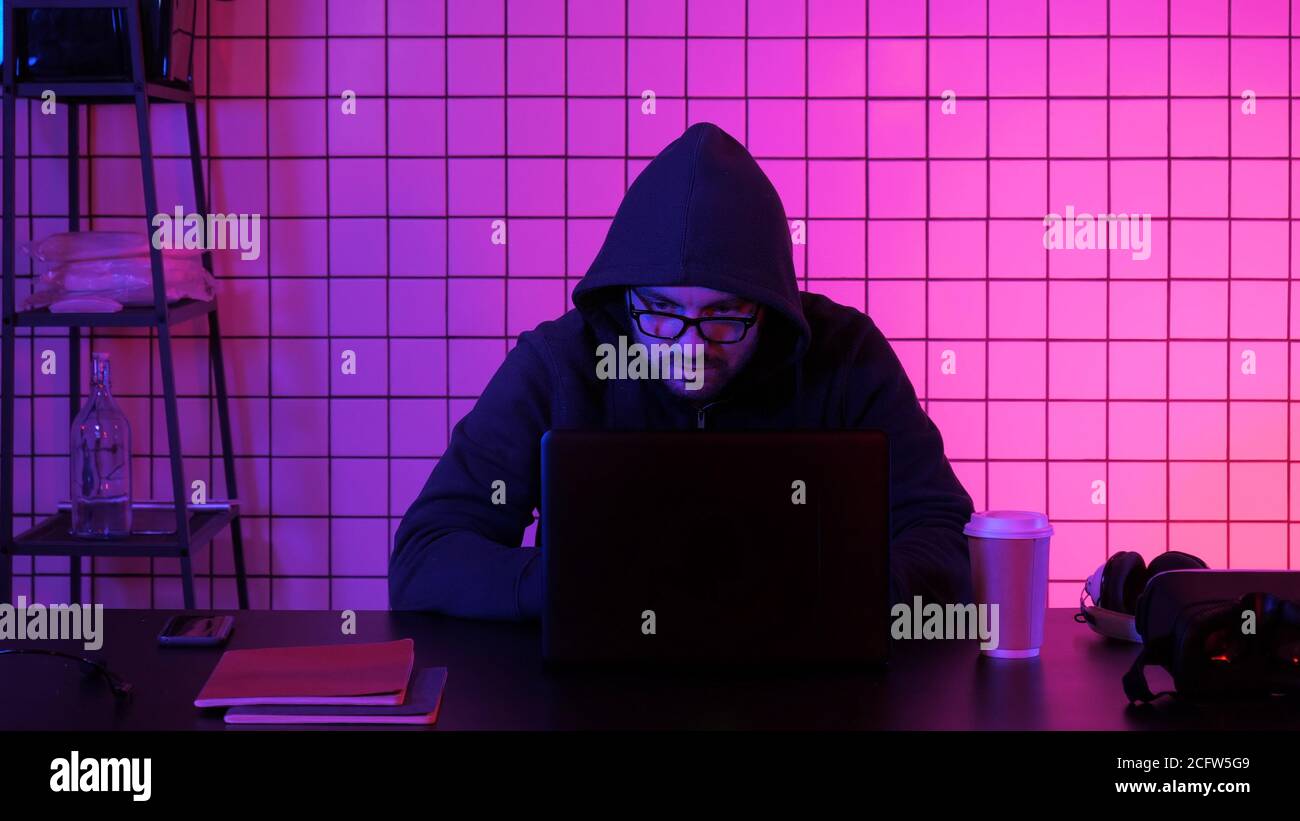 Giovane hacker finanziario maschile in ufficio seduto a lavorare su un computer portatile. Foto Stock