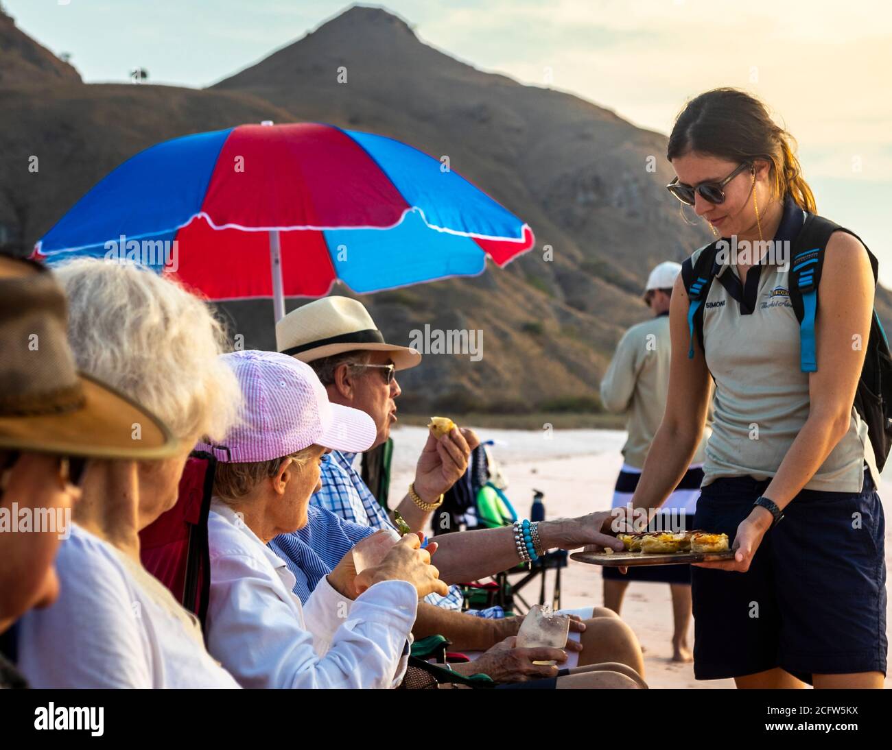 Picnic sulla spiaggia rosa di Pulau Padar. Le bevande in spiaggia sono accompagnate da tartine di formaggio di capra Meredith con cipolle caramellate. Crociera con fuoco e draghi del vero Nord, Isole Sunda, Indonesia Foto Stock