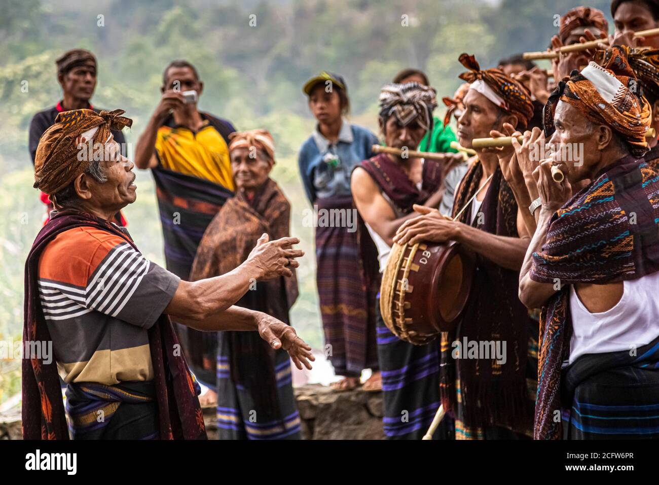 Gli spettatori osservano l'ensemble di flauti di bambù mentre il direttore guida il batterista e i flautisti con un gesto della mano esteso, villaggio di montagna Wologai vicino a Moni, Flores, Indonesia. Foto Stock