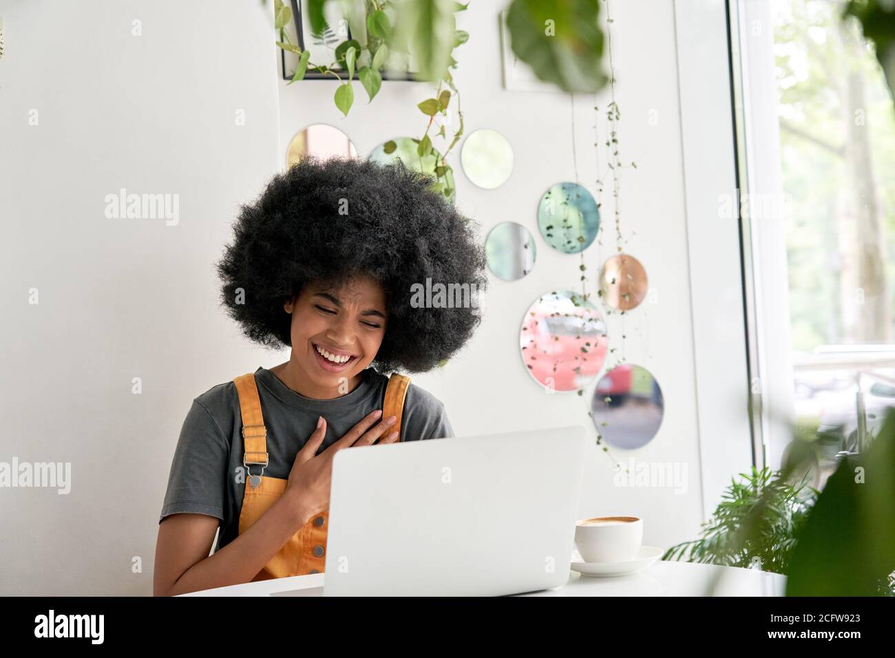 Felice studente di signora africana che usa il computer portatile ridendo seduto al tavolo nel caffè. Foto Stock