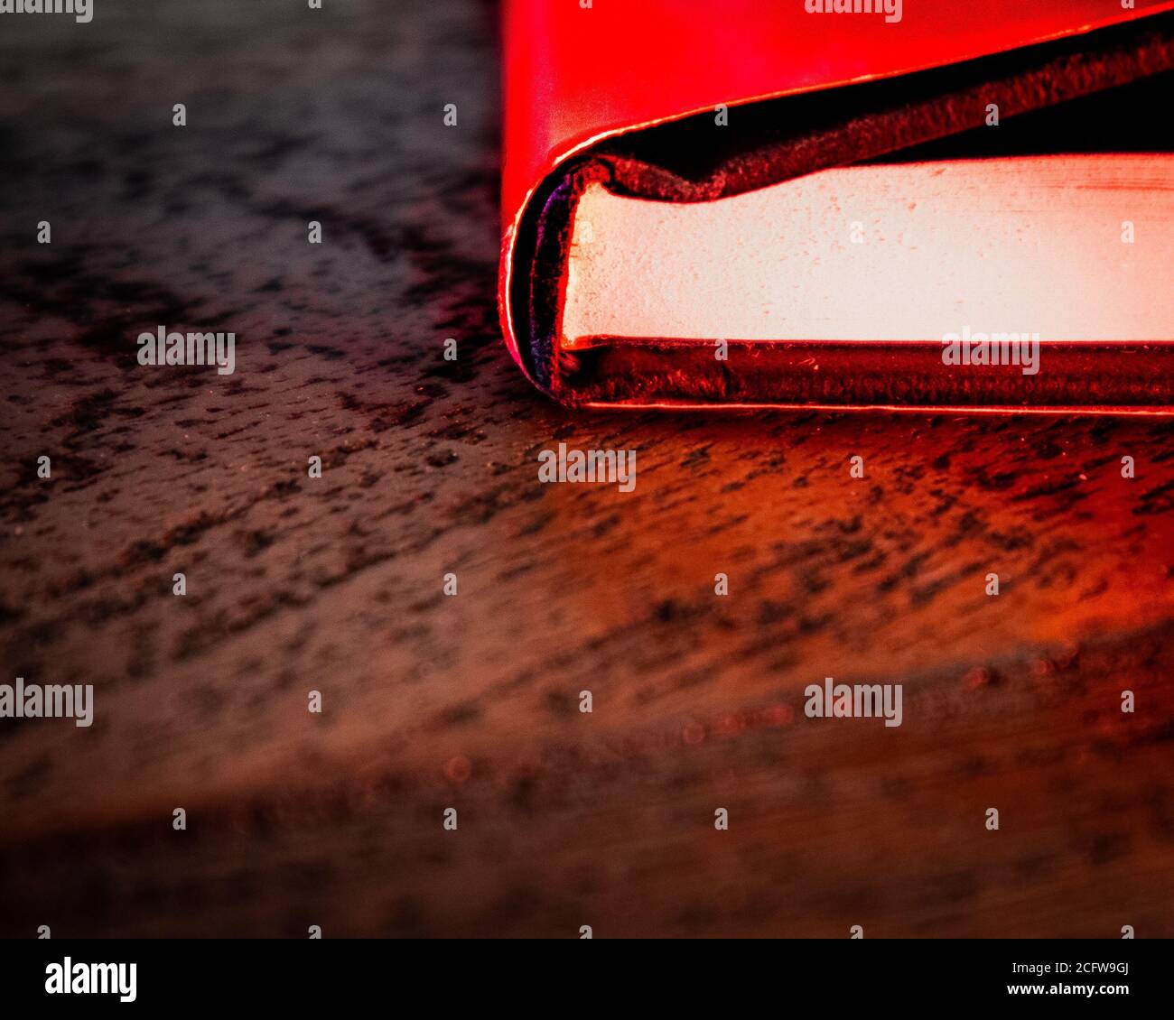 Un primo piano della colonna vertebrale di un libro rosso su un tavolo di legno con illuminazione rossa prominente Foto Stock