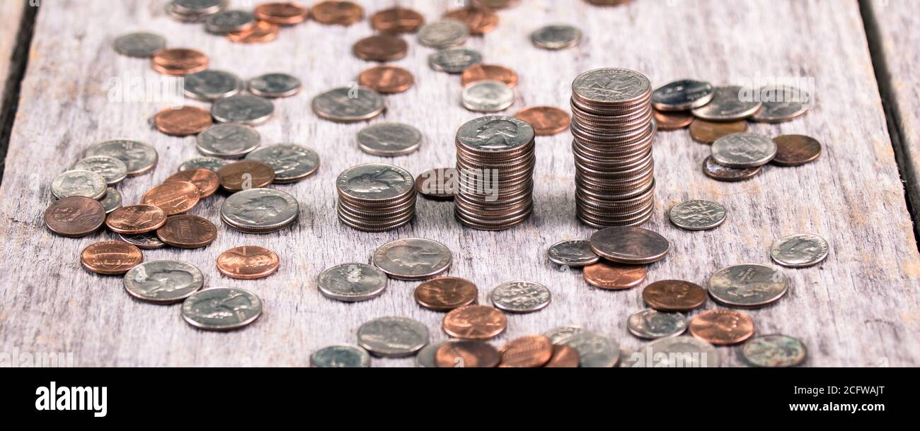 Pile di quarti su un vecchio tavolo di legno in mezzo sparso monete / concetto di crescita degli investimenti Foto Stock