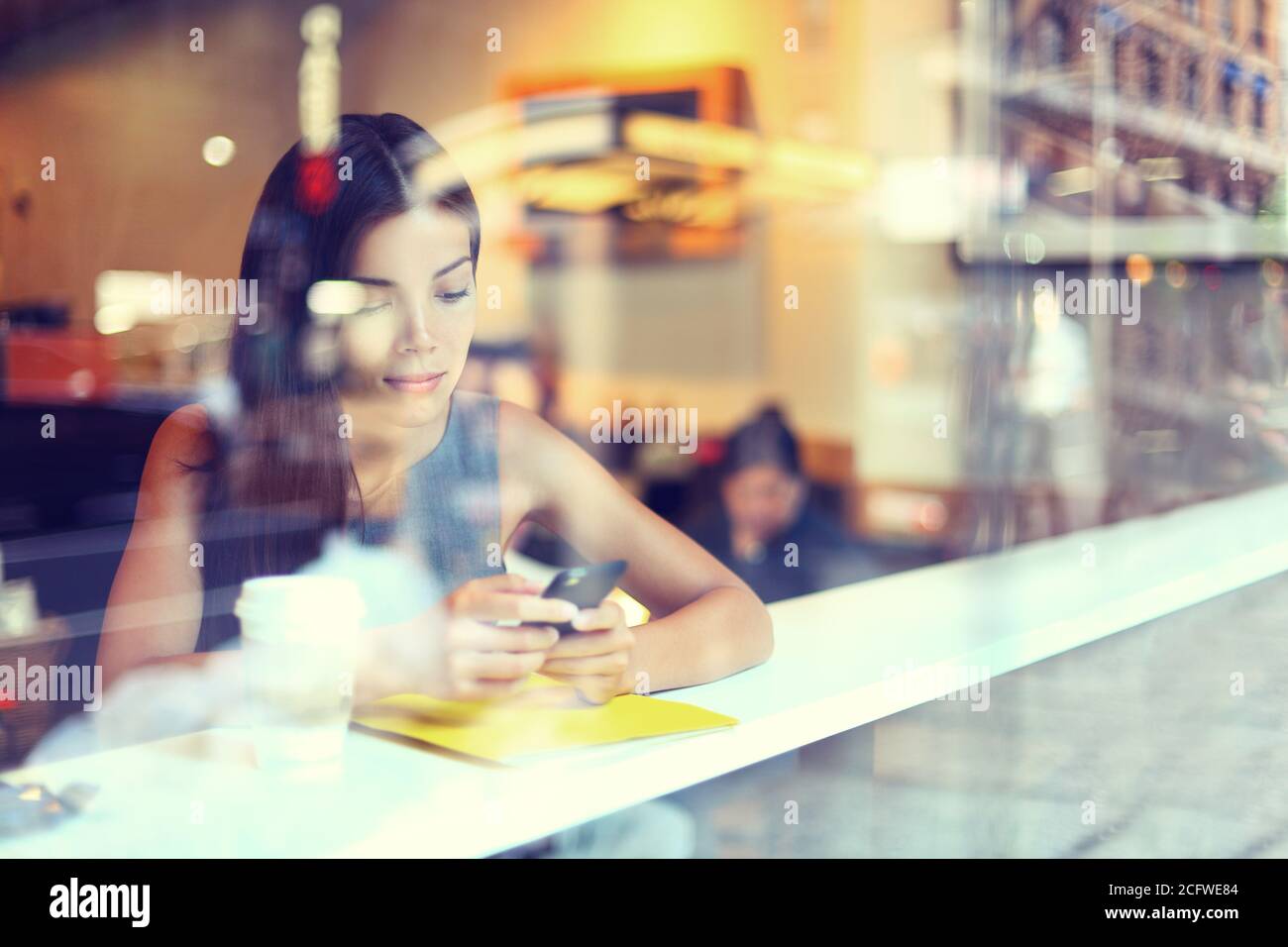Cafe city lifestyle donna al telefono di bere il caffè texting messaggio di testo sullo smartphone app seduta indoor nel quartiere alla moda di urban cafe. Cool giovani misto moderno Foto Stock