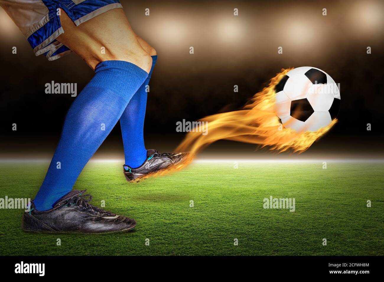 Giocatore di calcio che calcia un calcio fiammeggiante in volo in uno stadio. Foto Stock