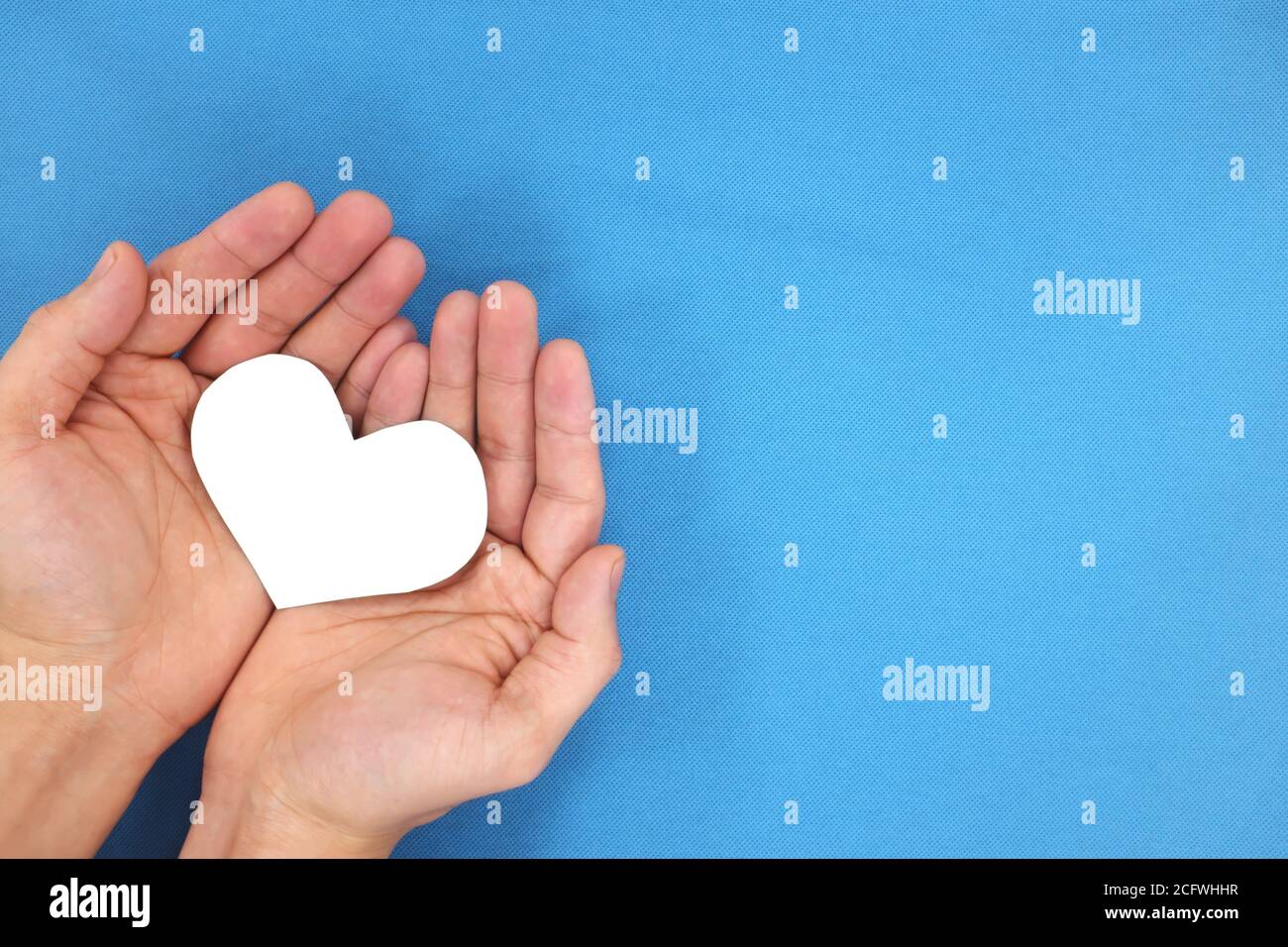 Mani maschili che tengono un cuore bianco nella vista dall'alto di sfondo blu. Concetto di gentilezza, carità e compassione. Foto Stock