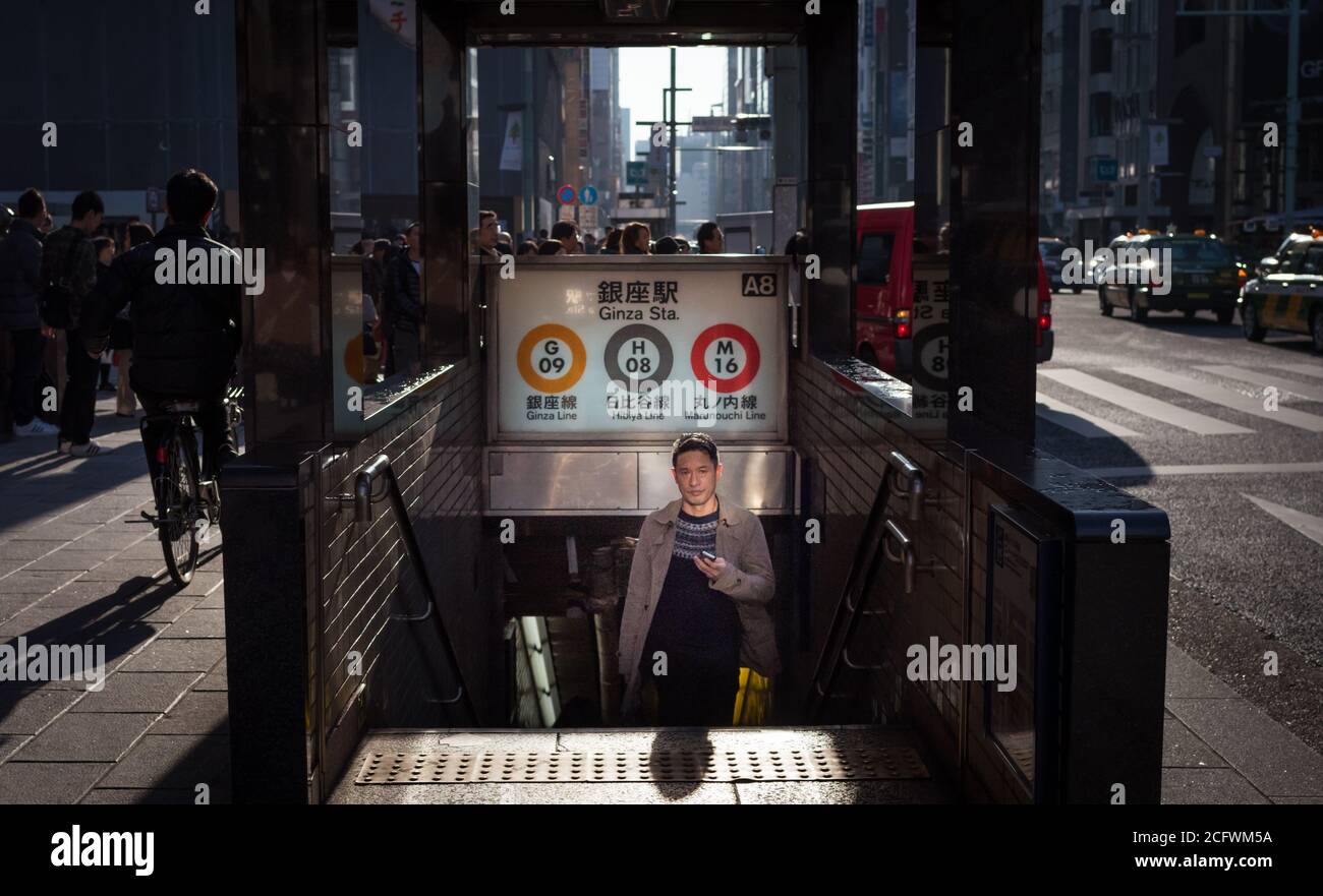 Ginza, Tokyo / Giappone - 23 dicembre 2015: Un uomo giapponese emerge da una stazione metropolitana/ferroviaria che tiene un cellulare/cellulare a un cit occupato Foto Stock