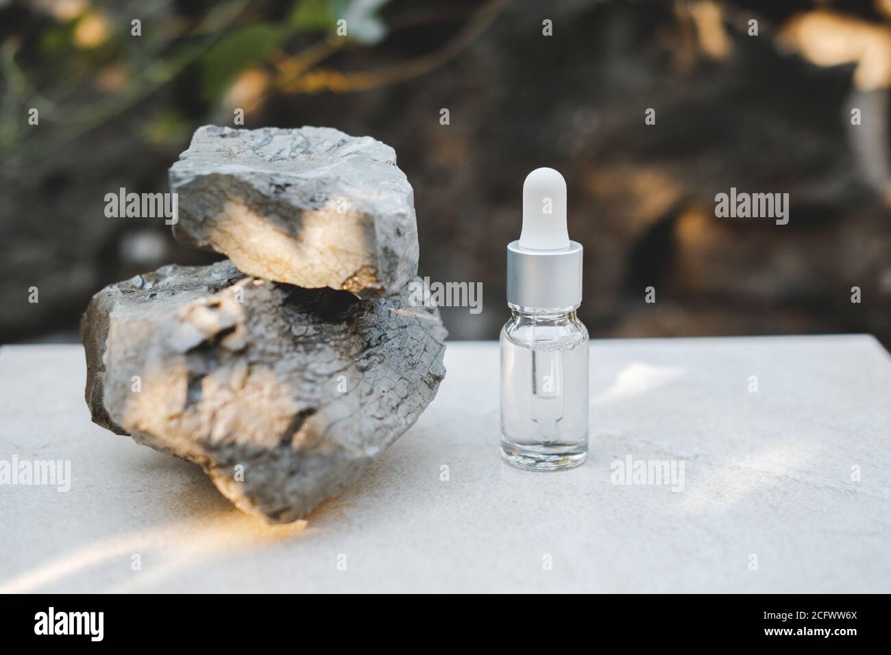 Bottiglie di siero trasparente accanto a pietre naturali contro una parete grigia con luce naturale. Stile alla moda. Trucco cosmetico. CopySpace Foto Stock