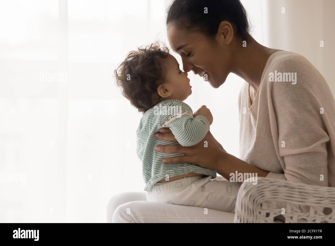 Sorridente giovane mamma afroamericana che tocca i nasi con carino capretto. Foto Stock