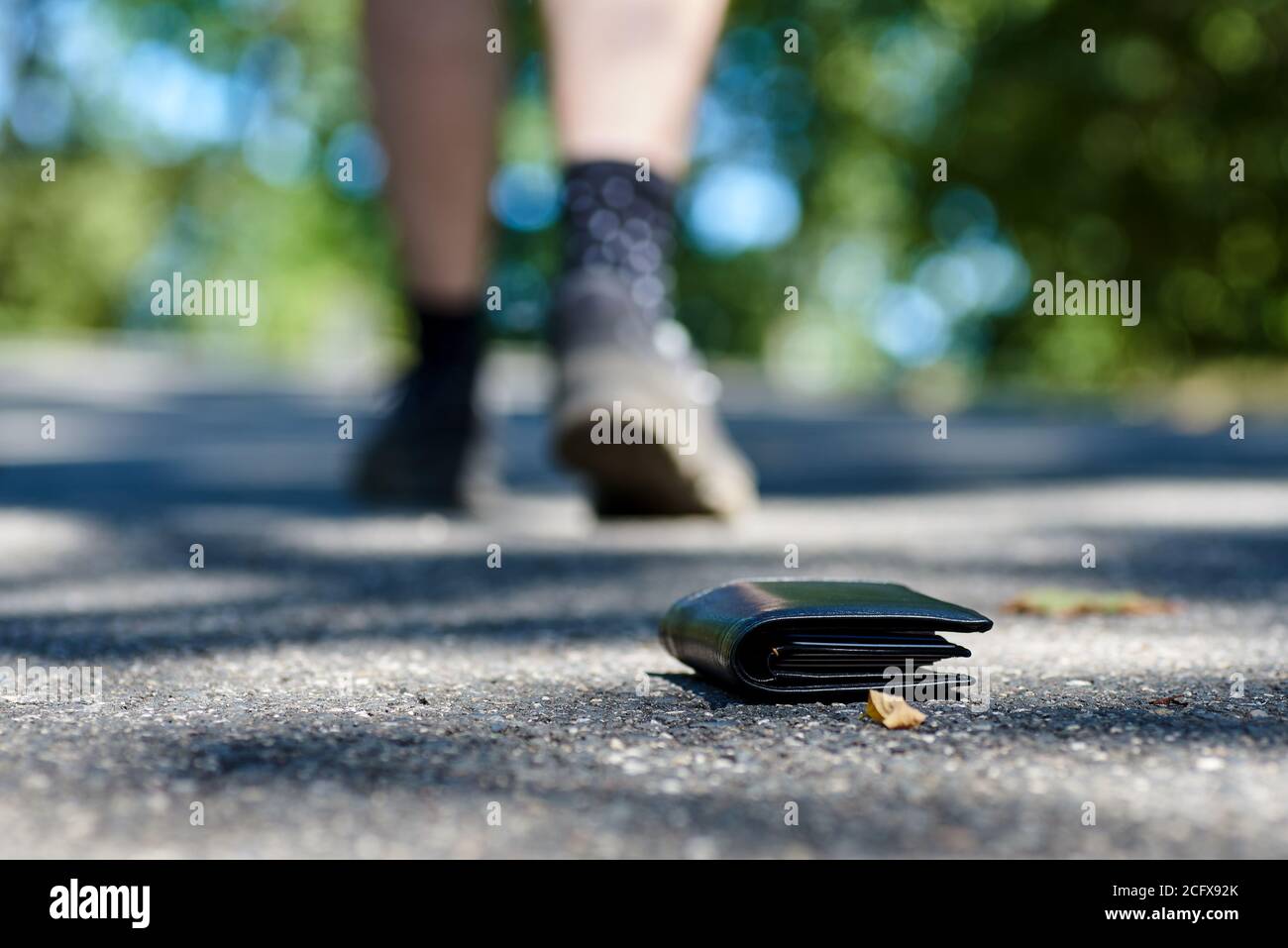 Foto del marciapiede e delle gambe di un uomo che ha perso un portafoglio in pelle nera mentre cammina Foto Stock
