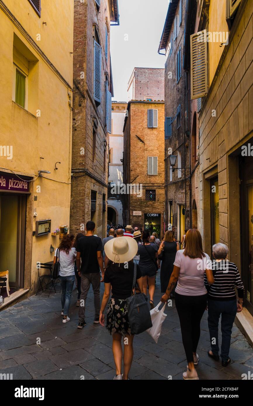 Una donna con un grande cofano soleggiato attraversa la stretta Via di Calzoleria, nella famosa città storica di Siena, Toscana, Italia. La strada conduce... Foto Stock