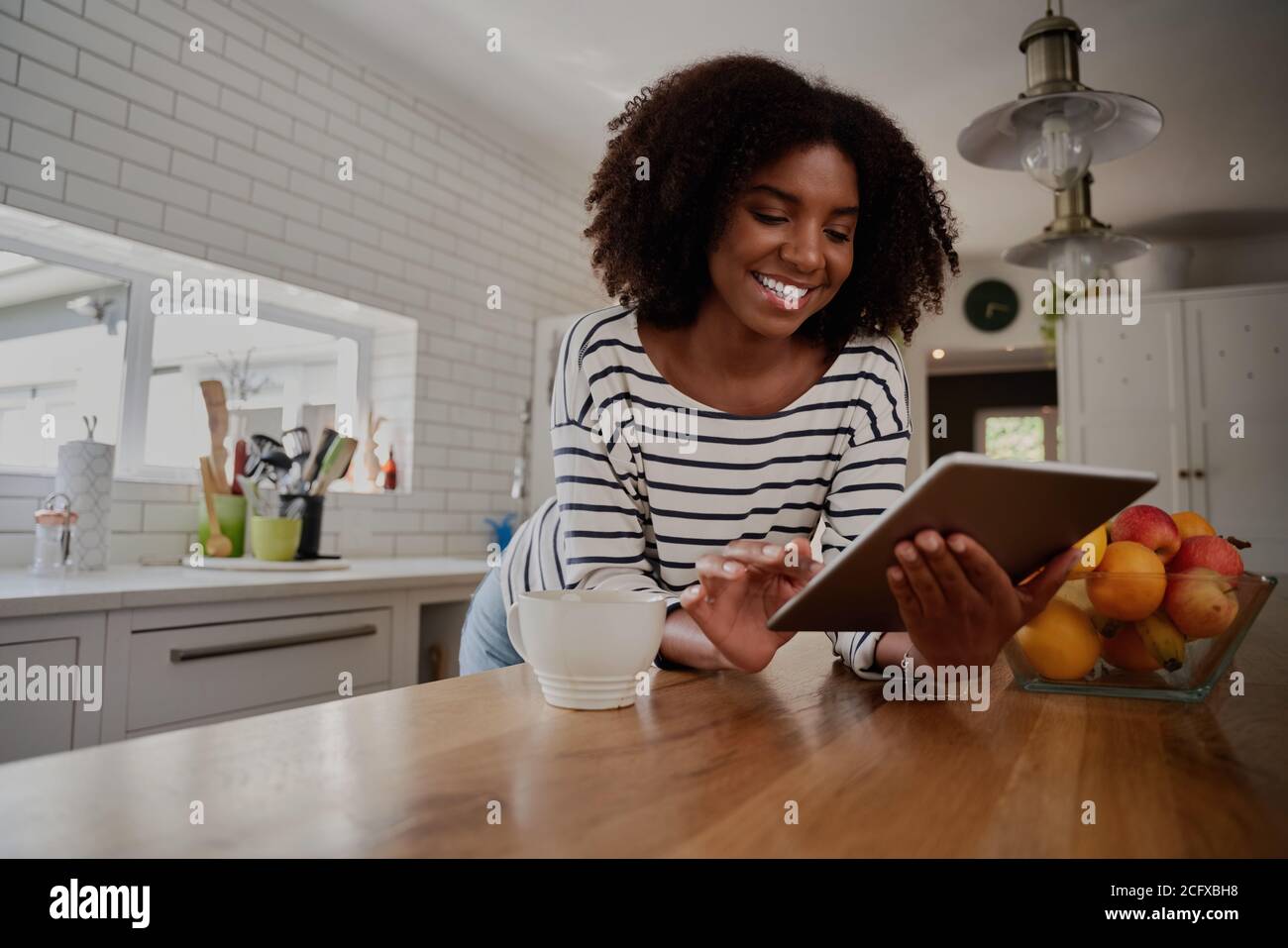 African American Woman in piedi in cucina appoggiandosi sul contatore usando tablet digitale che guarda le ricette online Foto Stock