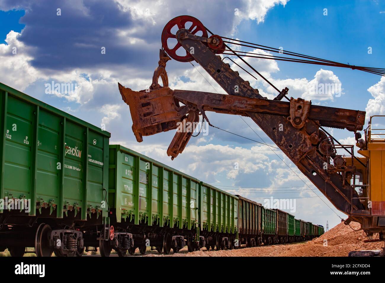 Estrazione e trasporto di minerali di alluminio. Attività minerarie aperte. Caricamento di argilla bauxite con escavatore elettrico nel treno tramogge. Foto Stock
