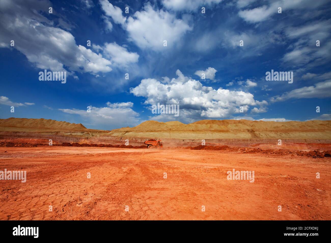 Estrazione e trasporto di minerali di alluminio. Cava di argilla bauxite. Miniera a taglio aperto. Dumper da cava Orange Hitachi. Su cielo blu con nuvole. Foto Stock