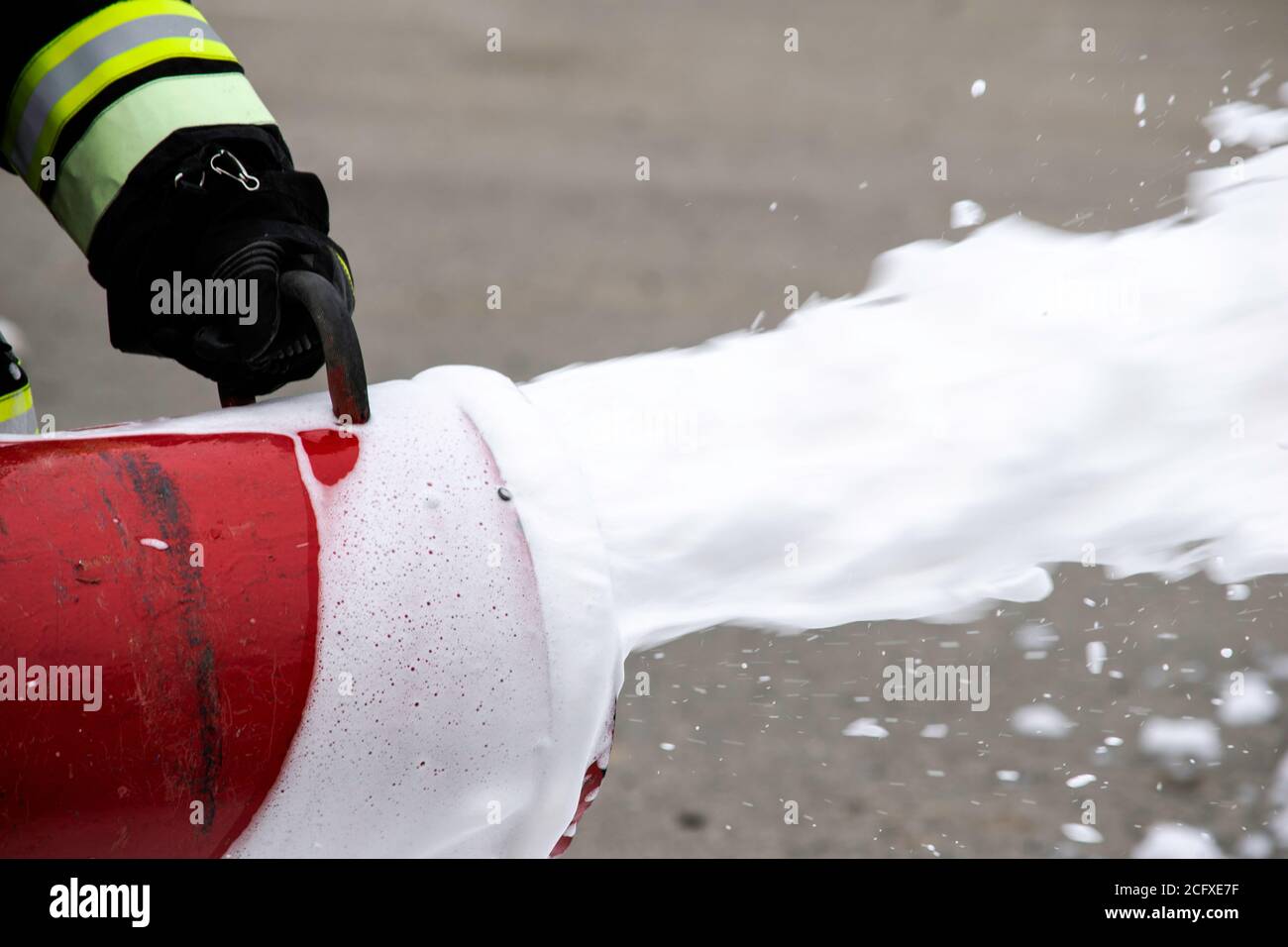 Fornitura di schiuma dal generatore di schiuma, schiuma antincendio vola dal generatore di schiuma, che mantiene il vigile del fuoco in abiti da combattimento Foto Stock