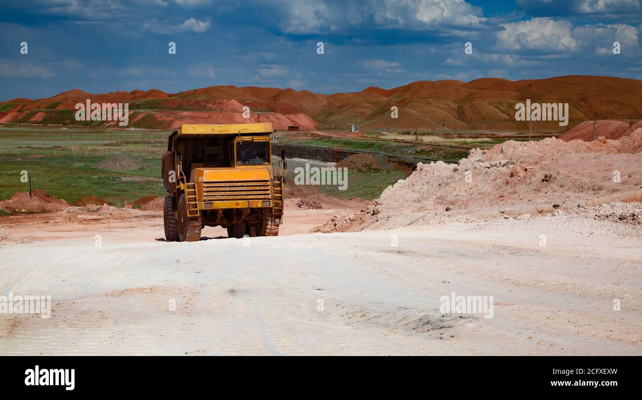 Estrazione e trasporto di minerali di alluminio. Miniera a taglio aperto di bauxite. Camion di cava gialla sulla strada bianca sul cielo blu con le nuvole nel giorno d'estate. Cumuli di scorie Foto Stock